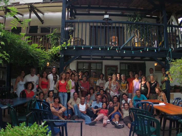 Grande grupo de pessoas no pátio de uma casa com varanda de madeira